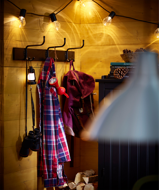 Стена със закачалки с окачени дрехи, над която светят лампи
