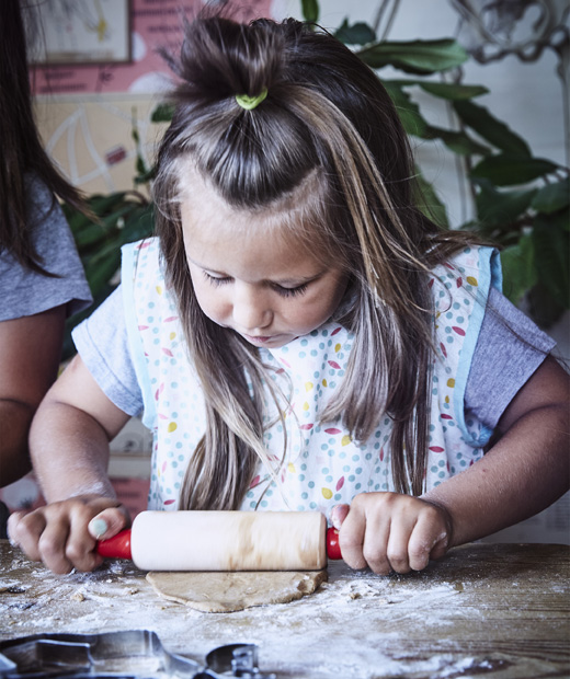 Дете точи тесто с точилка на маса с брашно.