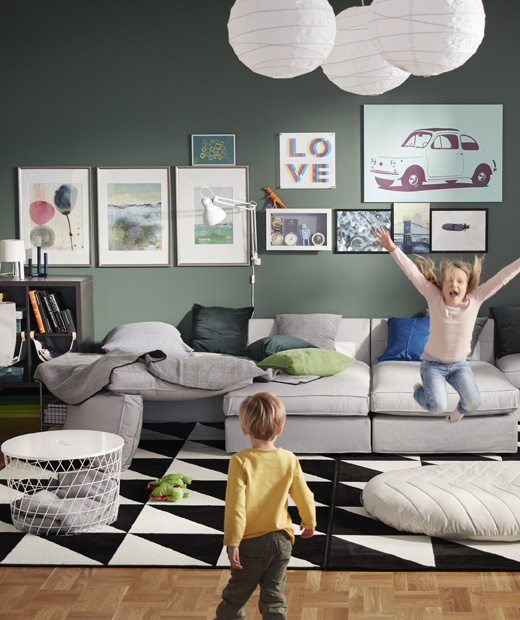 Зелена дневна с голям сив модулен диван и две играещи си деца.