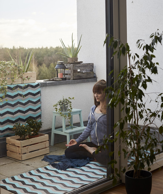 Ева практикува йога на постелка на балкон с растения.
