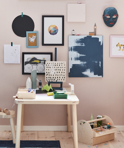 Картини и рисунки, поставени на розова стена над дървено бюро.