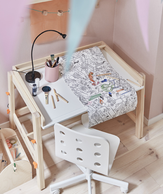 Ролка с хартия за оцветяване върху детско бюро с бял стол до розова стена.