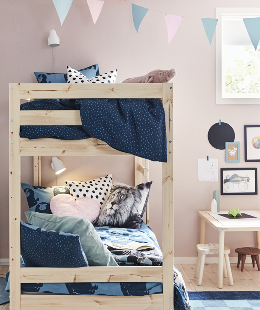 Дървено легло на два етажа в детска стая със сини завивки и розови стени.
